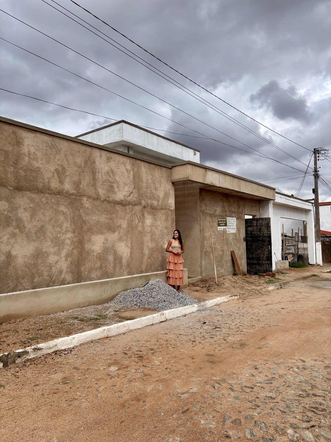 Irla Timbó em frente à fachada de uma obra acompanhada pelo escritório